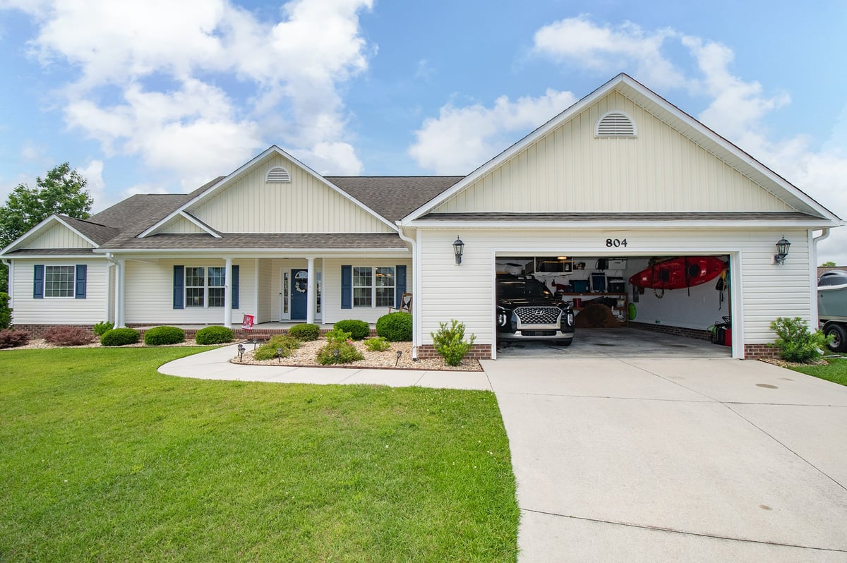 Single-story white suburban house with attached two-car garage, manicured lawn, and driveway on a clear day