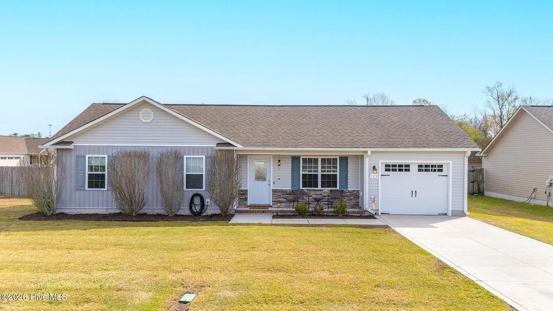 Single-story gray house with white garage, front porch, and large green lawn on a clear day