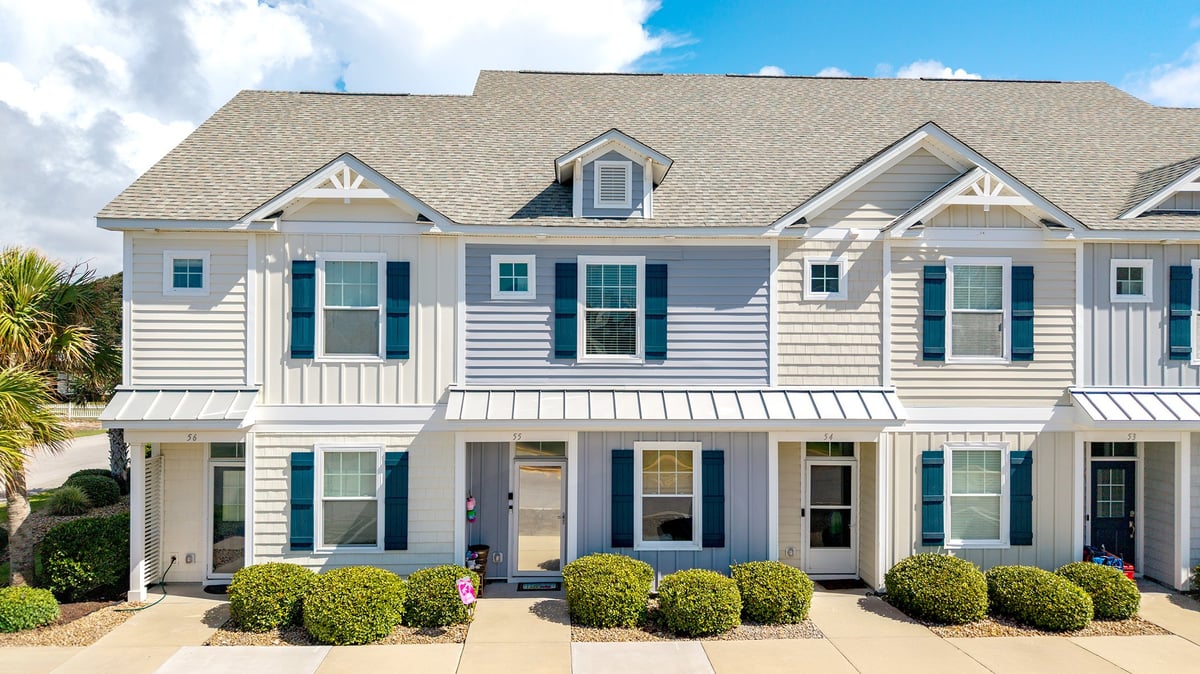 Row of modern white townhouses with blue-gray shutters, dormer windows, and manicured hedges in front
